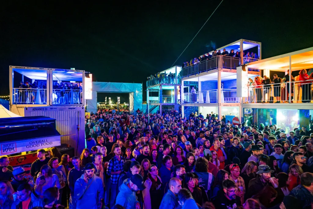 Nočný dav pred zónou IQOS Curious City na Pohode, streetfood BratNam a ľudia na balkónoch kontajnerovej stavby