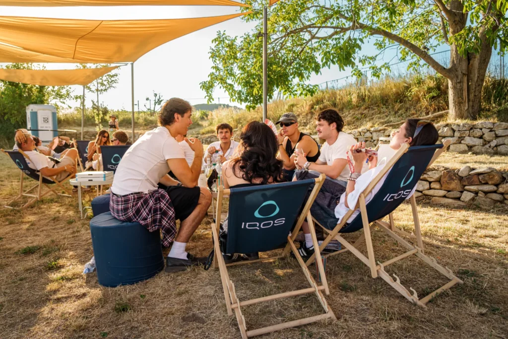 Návštevníci relaxujú v ležadlách IQOS pod tieniacou plachtou v zóne Curious City na Ženy Víno Funk