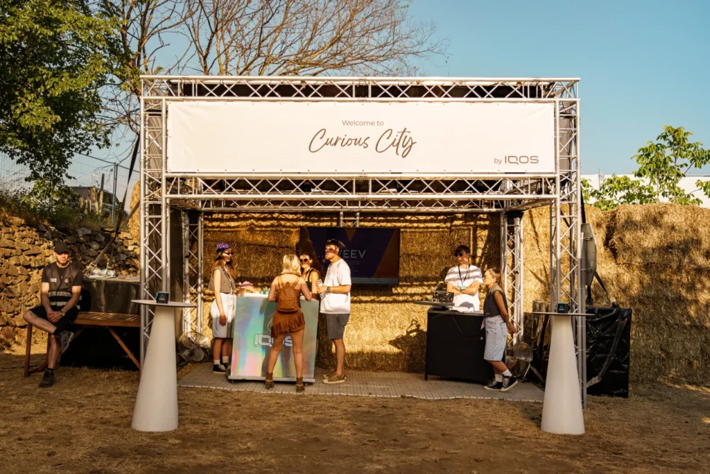 Vstupný pult zóny IQOS Curious City na Ženy Víno Funk s nápisom Welcome to Curious City a holografickým IQOS barom