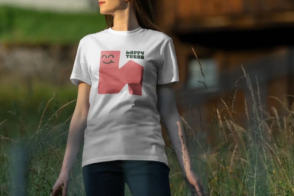 Žena v prírode oblečená v bielom tričku s ružovým maskotom dážďovky Happy Terra