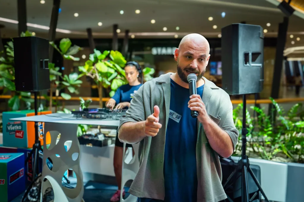 Moderátor Pablo s mikrofónom hajpuje dav na evente Tipos The Game, v pozadí DJ pult