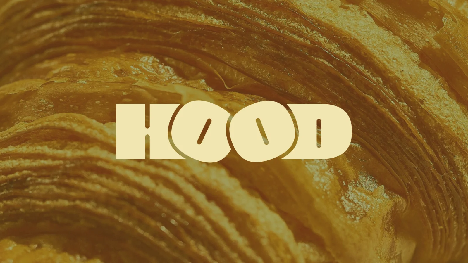Krémové logo bistra HOOD na detailním záběru zlatavého vrstveného těsta